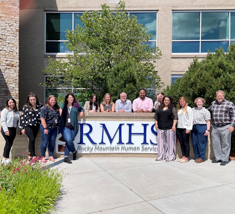 Image of RMHS building and sign, surrounded by happy staff members