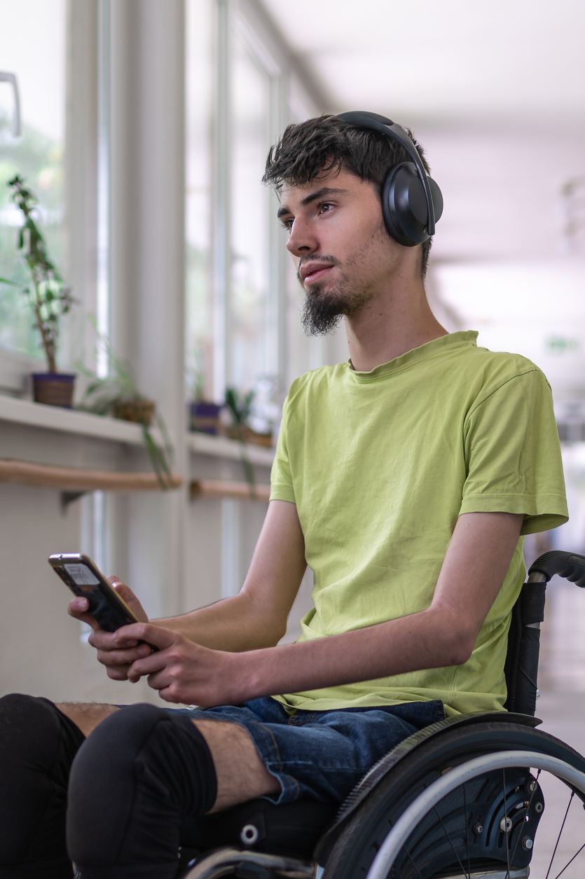 Teenager in his wheelchair holding his digital device while listening to headphones.