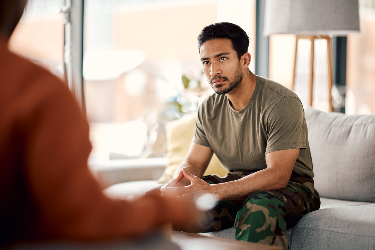 Hispanic veteran sitting on the couch receiving consult and support.