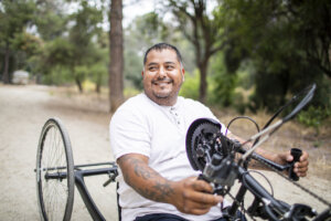 A Hispanic man riding his handcycle on a treelined path.
