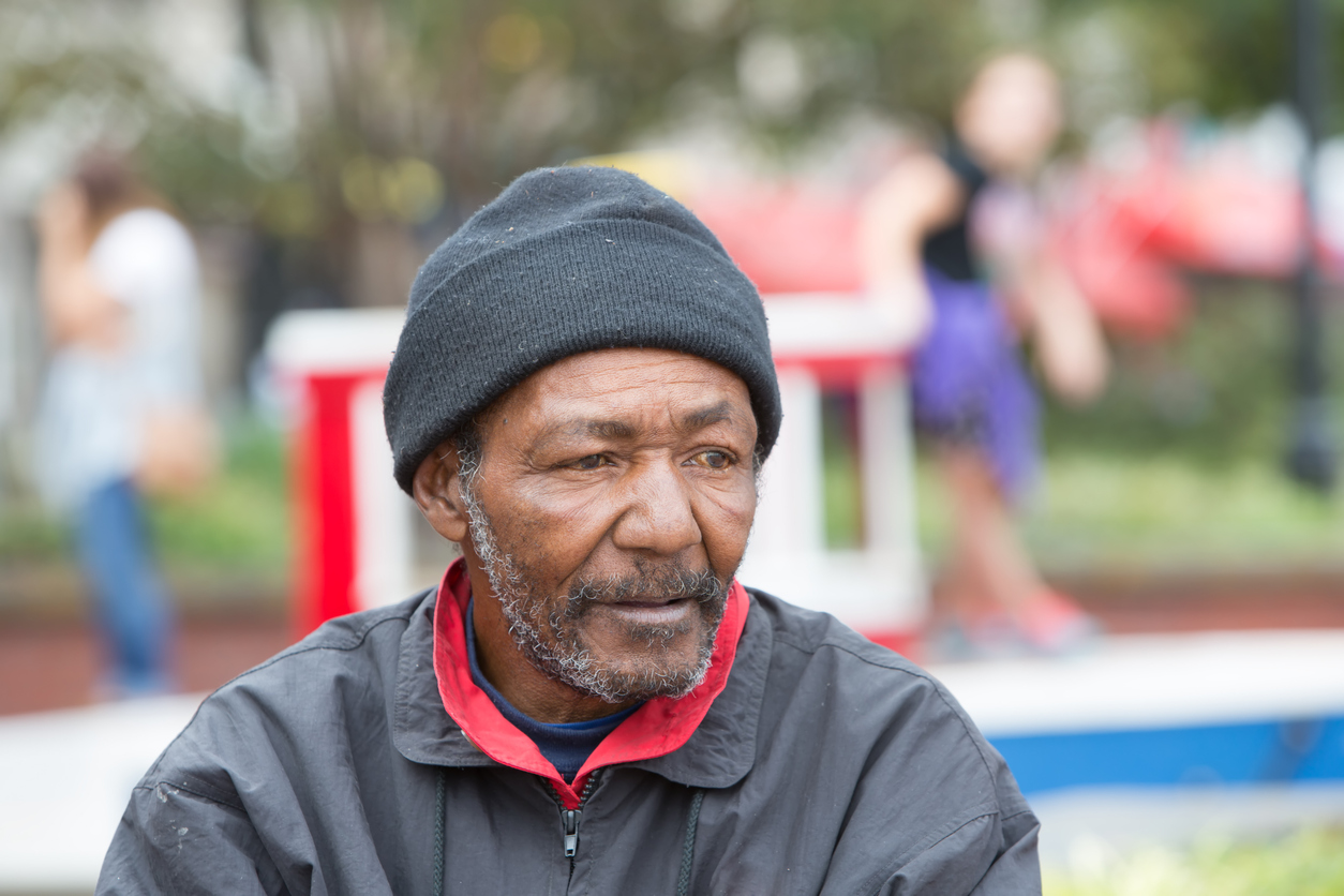 An older man struggling with housing insecurity sitting outside.