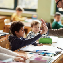 Child and teacher high fiving in a classroom.