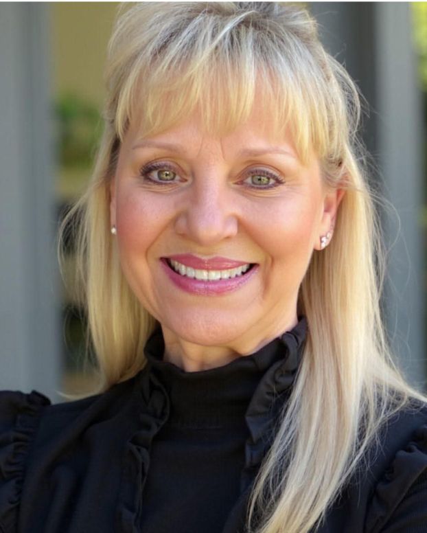 A woman smiles in a headshot with blonde hair and wearing a black blouse