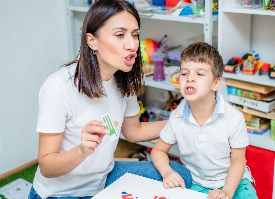 A young boy is in a play setting with an adult. They make faces as if they are sounding out words together