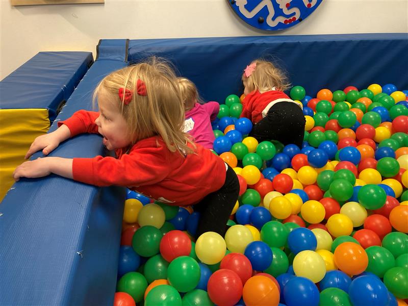 Young girls play together in a large ball pit surrounded by foam padding