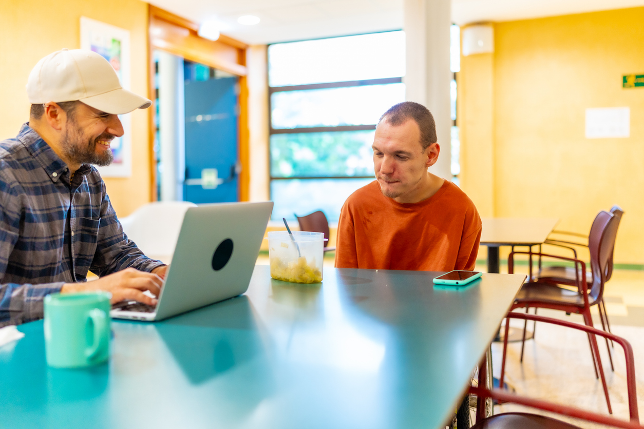 Disabled man and colleague working in the cafeteria of coworking Cauasian adult man with disability and case manager working together